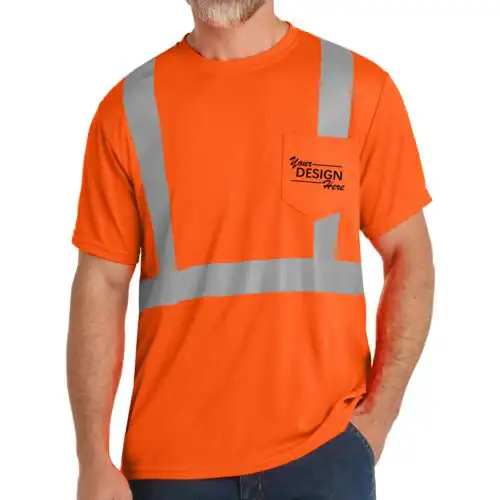 A man in NY wears an orange short-sleeve safety T-shirt with reflective silver stripes and "Your Design Here" on the pocket. Perfect for custom T-Shirts Manhattan & Long Island, he stands casually with one hand in his pocket.